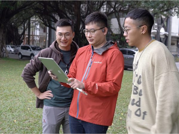 榕易迷路 AR Maze — testers in NCKU Banyan Garden hold a tablet showing the AR hedge maze overlaid on real grass.