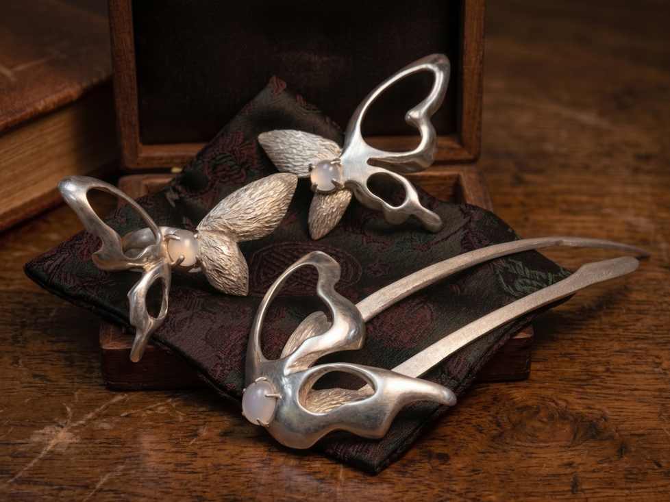 Liang-Zhu jewelry set — butterfly hairpin and brooches arranged on dark wood with a leather book.