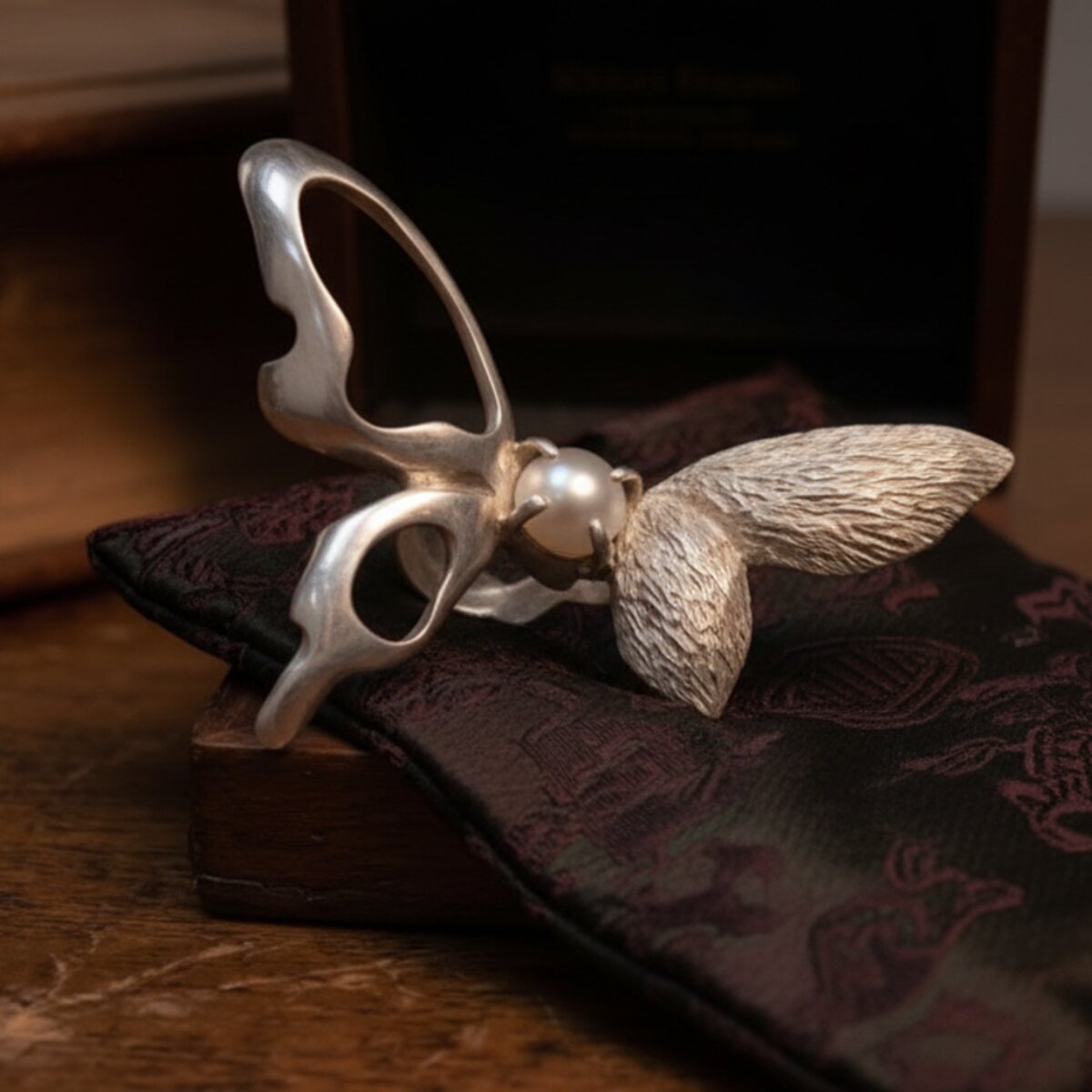 The ring piece, shown from a low rear angle, with a small pearl set in the centre of a butterfly form.