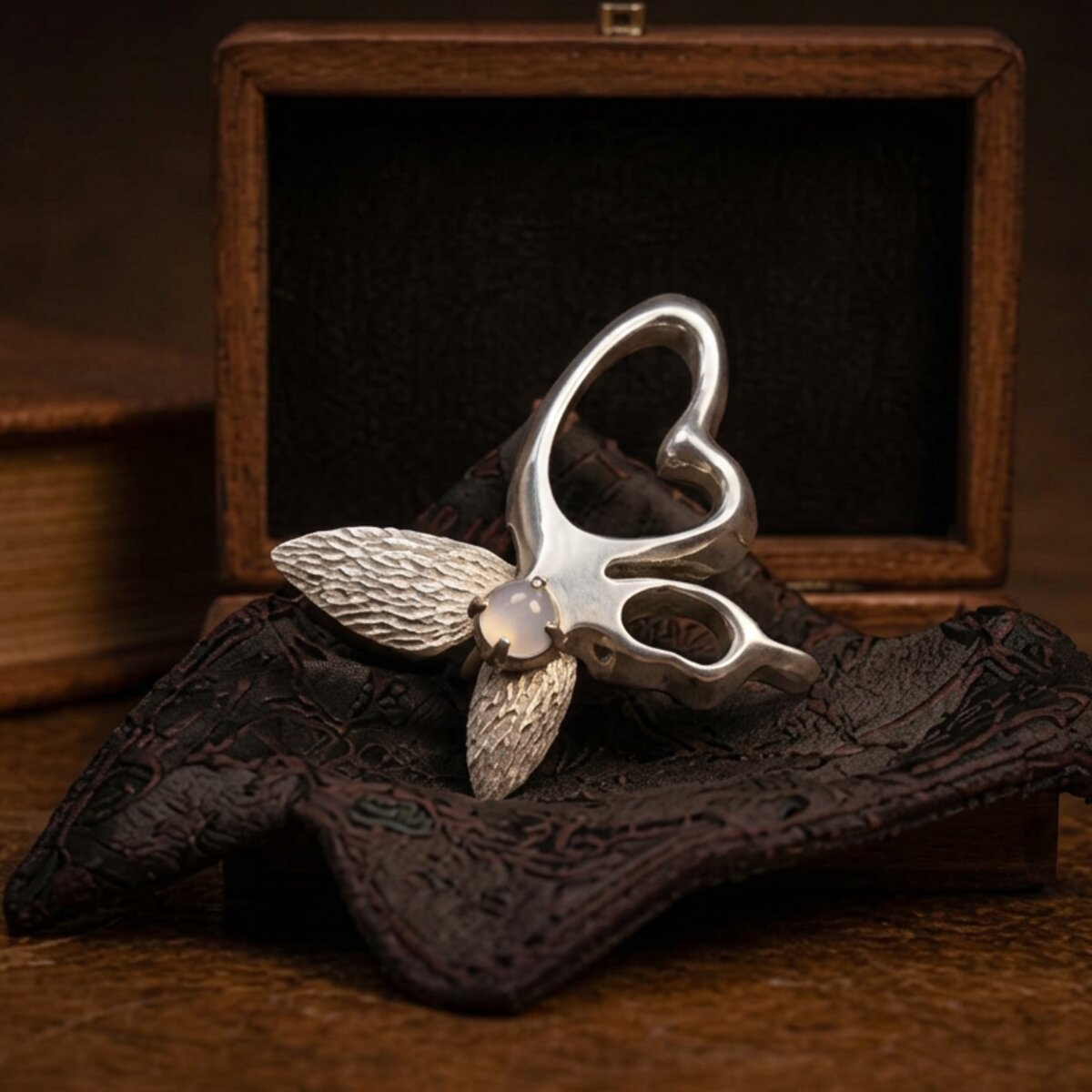 The butterfly brooch, shown from a low angle, with finely textured wings and a moonstone at the centre.