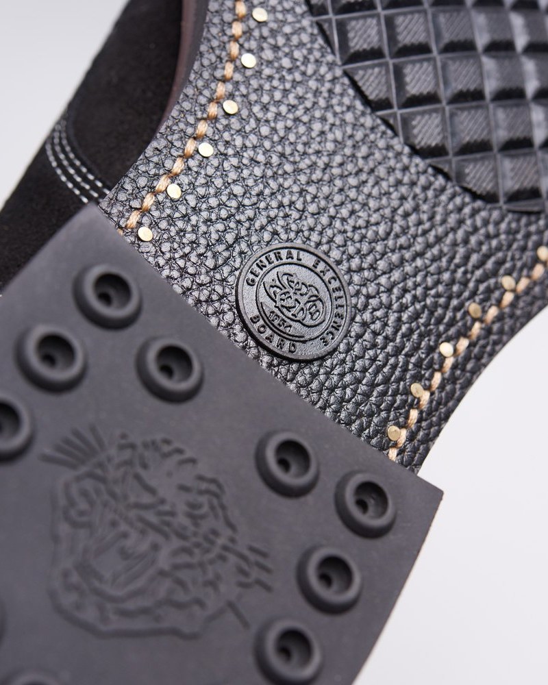 A macro detail of the Officer Boots' custom outsole and footbed: a tooled rubber outsole with circular tread cups and an embossed tiger crest, a 'General Excellence Board' leather medallion, decorative brass studs running along an edge-bound seam, and quilted insole texture above.