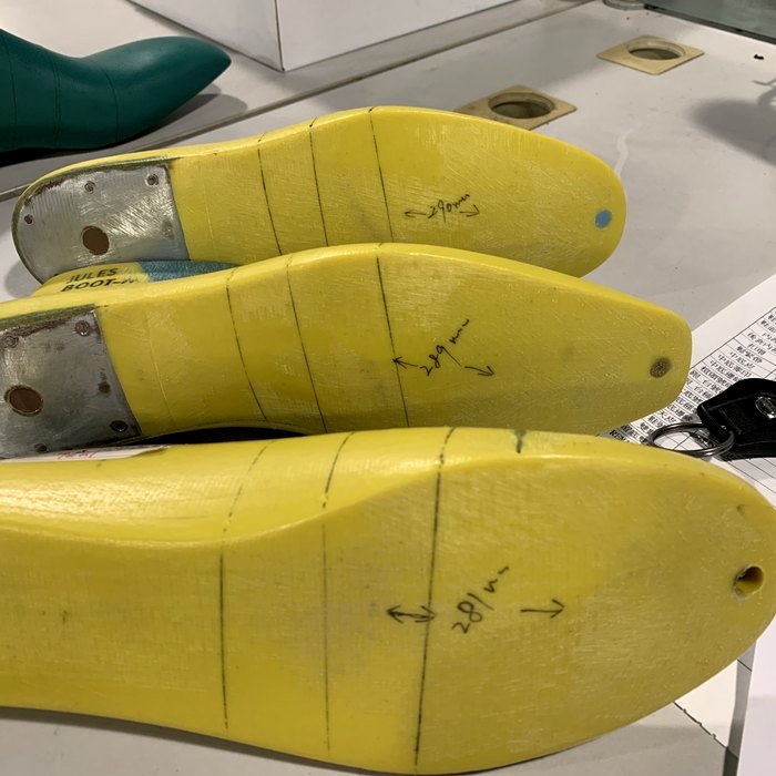 Three yellow shoe lasts hand-annotated with millimeter markings (29mm, 28mm) and labeled 'JULES BOOT' on a workshop shelf — real client-supplied lasts.